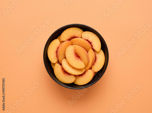 Top view of fresh sliced peach in a dark bowl on a peach orange background
