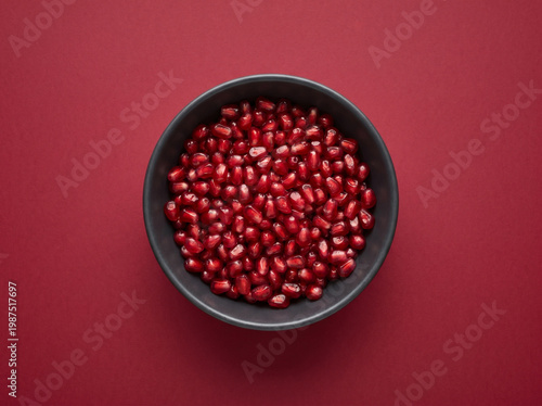 Top view of fresh pomegranate seeds in a dark bowl on a red background