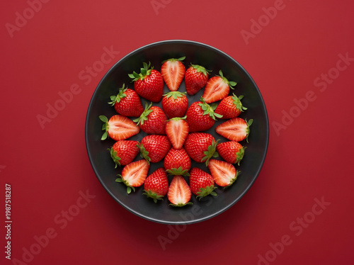 Top view of fresh halved strawberries in a dark bowl on a red background