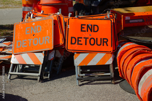 Φωτογραφία Bright orange End Detour signs and stacked traffic cones rest on pavement at a road construction site, conveying traffic control, temporary closure, and urban maintenance work in daylight