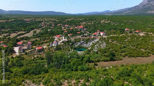 Aerial view of the Eye of the Earth, the Cetina River spring in Croatia, featuring the turquoise karst lake, village houses, and surrounding mountains