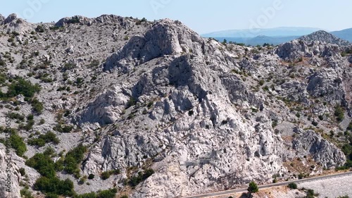 Aerial view of the rugged limestone peaks of Velebit mountain range near Tulove Grede, Croatia, featuring a scenic mountain road with traffic.