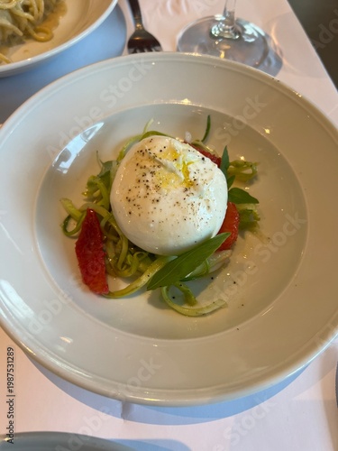 Fresh burrata cheese served with green pesto and tomatoes.

 A gourmet appetizer plate featuring a whole creamy burrata cheese ball on a bed of green pesto and sun-dried tomatoes, garnishe