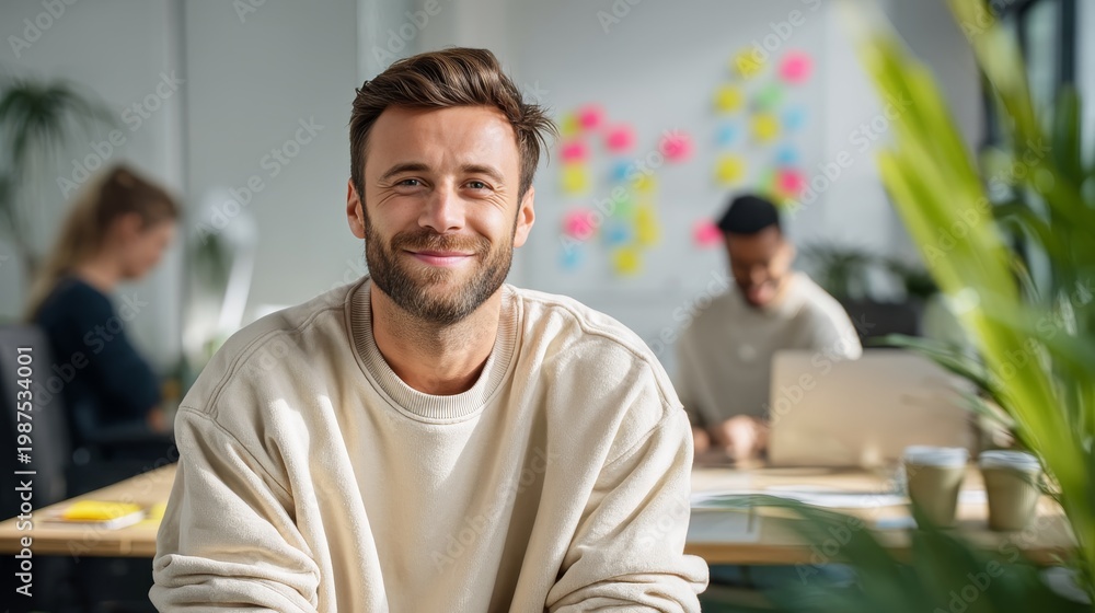 Fototapeta premium Smiling young man in modern office environment. Bright workspace enhances creativity and productivity. Professional atmosphere supports teamwork and innovation. Quality image for corporate use.