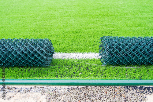 Synthetic grass sports field with rubber infill and chain link fence rolls, fencing installation during construction process