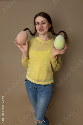 Young woman with pigtails on a blank background with Easter eggs in her hands