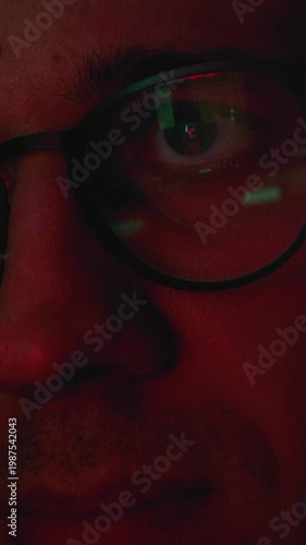 Portrait close up: man working at night looking at monitor, reflections in eyeglasses. Person stock market trader using laptop at office or home office. Business distance work, freelancer male