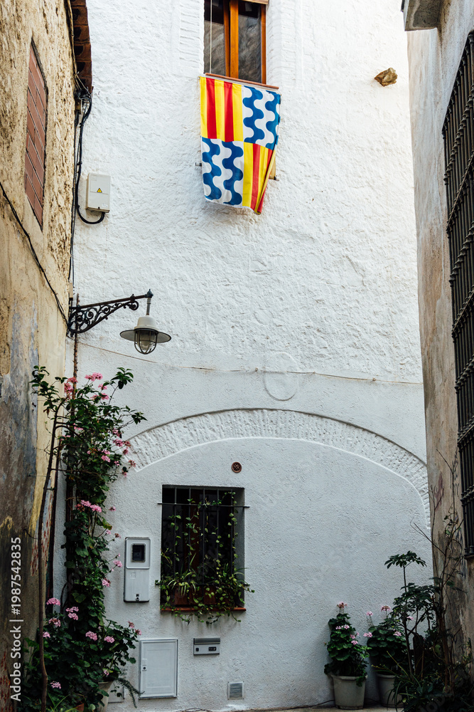 Fototapeta premium Street of the old quarter of Badalona with a lamppost and flag of the city in a window