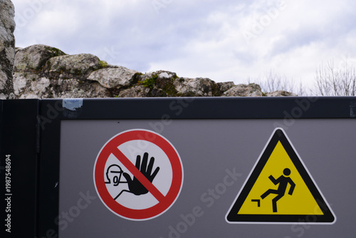 Industrial safety signage on a gray fence wall, including a no entry symbol and a falling hazard warning. Concept of danger, security, and workplace caution.