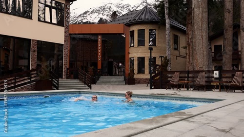 A mother and daughter happily swim in a hot pool in the winter in a forest high in the snowy mountains.