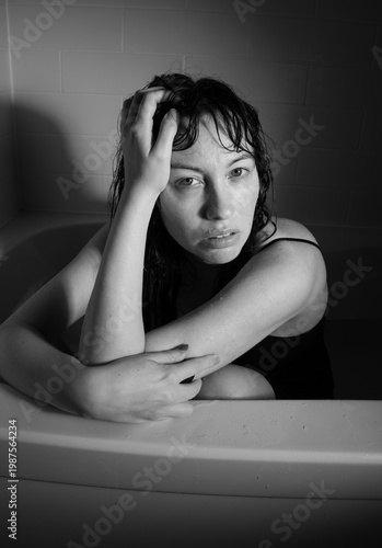 39-year-old woman in bathtub expressing distress, emotional exhaustion and vulnerability. Black and white moody self portraits with wet hair, dramatic lighting, raw human emotion.