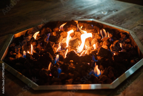 Gather around a fire pit in a winter setting. Flames dance among rocks as they share stories and enjoy snacks. Snow covers the ground, creating a cozy atmosphere