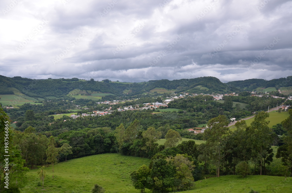 Obraz premium Scenic rural valley with small town and rolling green hills under cloudy sky