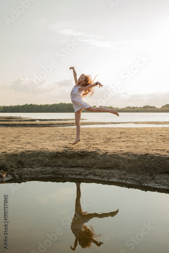 Beautiful little girl jumps on the sand on the river bank. Little ballerina girl is dancing on the nature. Kid and child on vacation. Selective focus