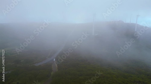 A winding road through the misty, wind-swept Paul da Serra plateau in Madeira, dotted with renewable energy turbines. An atmospheric drive.