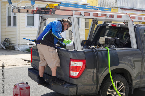 Foto Handyman standing on his pickup truck and looking into bed with ladders on top a
