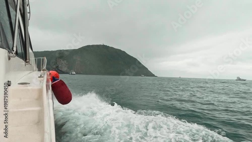 A motorboat fast sails across the sea during cloudy, choppy weather, as seen from the side. Waves splash in all directions