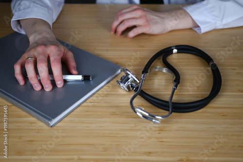High angle view of doctors hands lying on a table. One hand rests on the table and the other hand lies on a notebook assuming grabbing a pen 