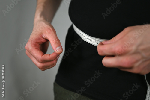 A man is holding a tape measure around his waist to measure his waist circumference. 