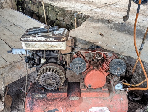 Canvas Print Old rusty air compressor machine sitting on a wooden floor outdoors