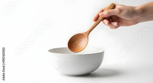 Close Up of Hand Holding Wooden Spoon Over White Bowl in Minimal Kitchen Scene