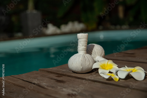 Set of  thai herbal heat bag for asian thai massage with flowers on wooden background front of the pool. Recreation and health care concept.  Selective focus.