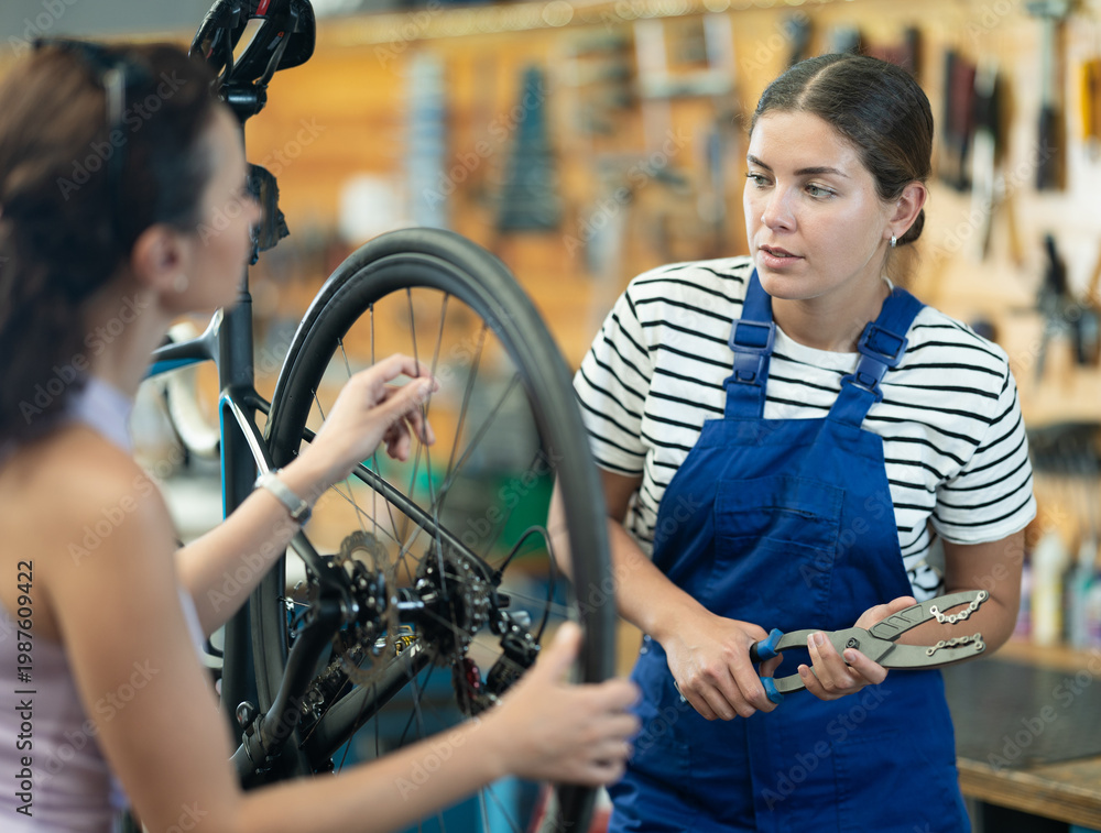 Obraz premium Young woman bicycle repair service worker in uniform advises female client