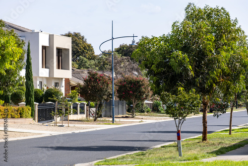 Schilderij op canvas a modern quiet street in Point Cook, Melbourne, featuring a street lamp, lush green trees, and contemporary suburban houses
