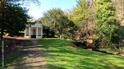 Cinematic view of a charming garden gazebo and a wooden footbridge over a gentle river within a historic Scottish estate