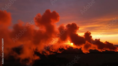 Sunset illuminates orange industrial smoke, casting long shadows across a distant, low landscape