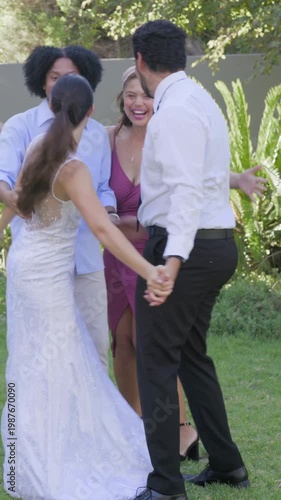 Vertical video: Stepping in friends congratulating and hugging newlyweds on lawn, with gown and tie