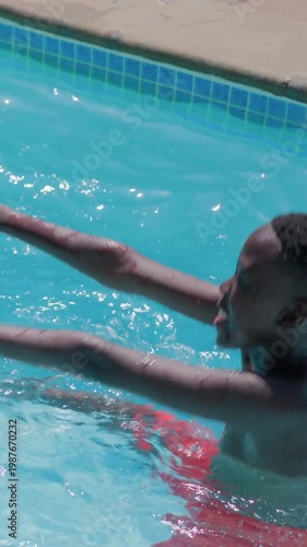 Vertical video: Playing boy in trunks reaching for drifting mat in home pool, adult saving, helping