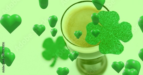 Drifting glossy green hearts circling stemmed glass holding frothy drink in studio, glitter clover