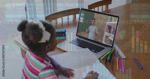 Child wearing striped shirt, white bows, studying at dining table with laptop, workbook, copy space