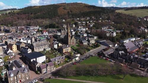 Aerial panoramic sweep over the traditional stone houses and rooftops of Peebles, capturing a prominent historic church tower and the scenic urban landscape of the Scottish Borders