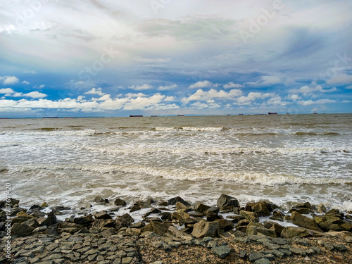 Granite rocks, ocean waves, and a few ships on the horizon under the cloudy sky of São Marcos Bay, on the coast of São Luís, Maranhão, Brazil.