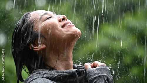 Young woman enjoying heavy rain with closed eyes outdoors