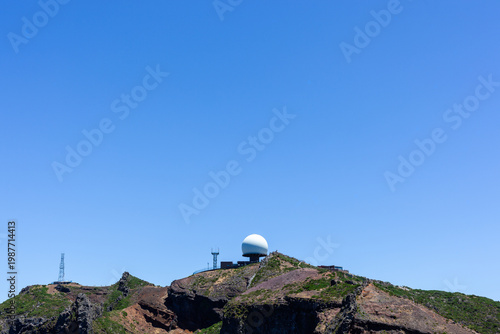 Pico do Areeiro radar stands on Madeira's mountain peak. Clear skies highlight rugged terrain of Vereda do Areeiro trail. Hiking destination offers panoramic island views.