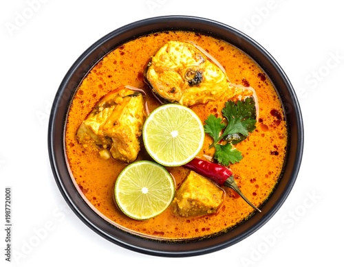 Top-down shot of a dark bowl filled with fish curry and garnished with lime slices, a red chili, and cilantro