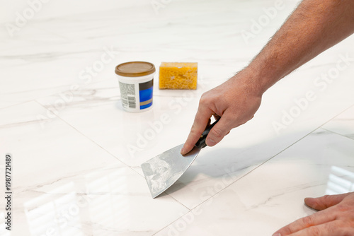 Foto Applying grout on ceramic tile floor using putty knife during installation