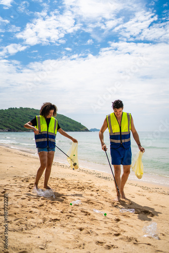 Two volunteers collecting plastic bottles and trash on a sandy beach. 