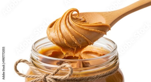 Creamy peanut butter on wooden spoon held over open glass jar against white background macro.