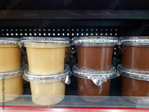 Peanut and chocolate spreads in transparent plastic cup packaging with sealed foil lids displayed on a store shelf. Creamy texture food product for bread spread, filling, topping. Retail and business