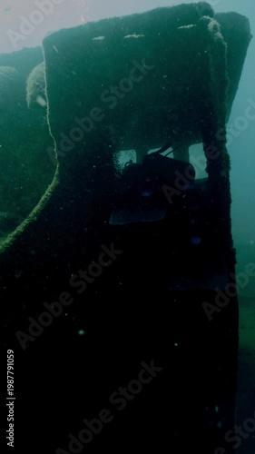 Diver swimming near a sunken boat covered in algae, exploring the mysterious underwater world