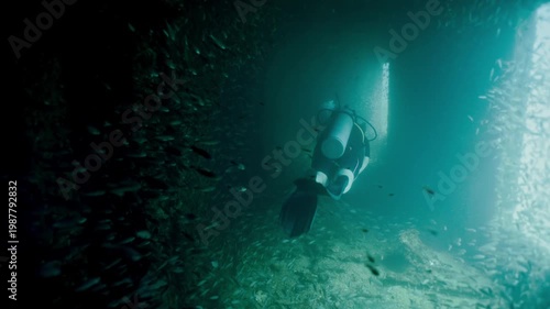 Brave scuba diver swimming through a dark sunken ship while exploring marine wildlife in deep ocean