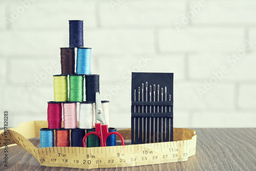 Colorful sewing thread spools stacked with needles, scissors, and measuring tape on a wooden table. Perfect for DIY, tailoring, and craft
