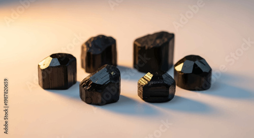 Six raw black tourmaline crystals displayed on a light surface with warm lighting.