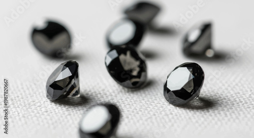 Close-up view of multiple faceted black gemstones, possibly black diamonds, scattered on a light textured fabric surface.