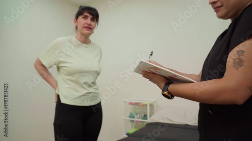 Woman with severe back pain describing symptoms to a physiotherapist taking notes in a clinic, highlighting concepts of injury, healthcare, and treatment