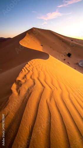 A sunlit desert landscape reveals a towering dune with rippling sand textures and a vibrant gradient sky at dawn